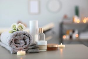 a spa setup with a towel, scented candles, creams, oils, and flowers on a table
