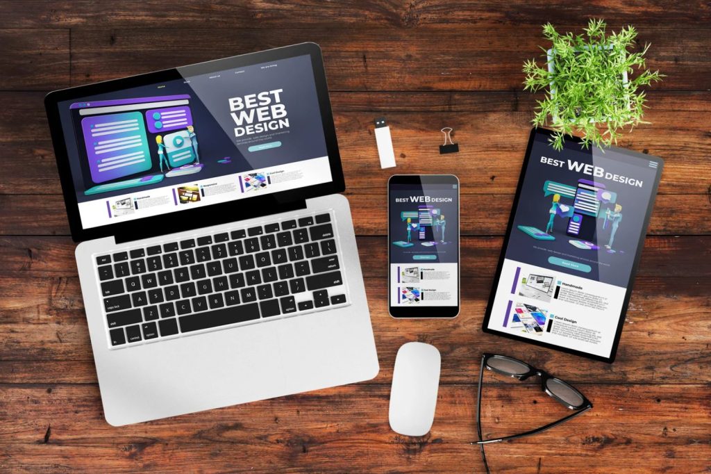 a web designer's table with website layout in laptop, tablet, & mobile phone.